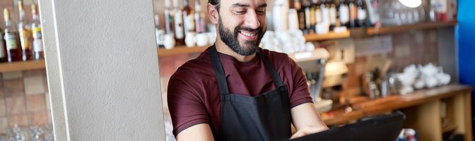 small business owner in apron at counter working at bar or coffee shop on computer
