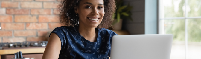 Positive motivated young female working on laptop smiling and looking at camera