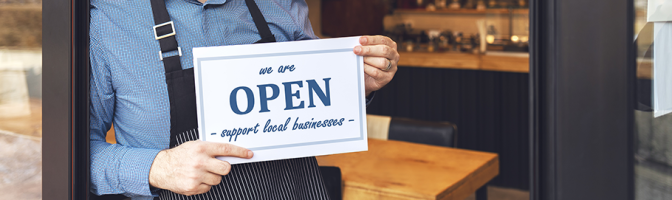 Small business owner smiling while holding open sign of restaurant