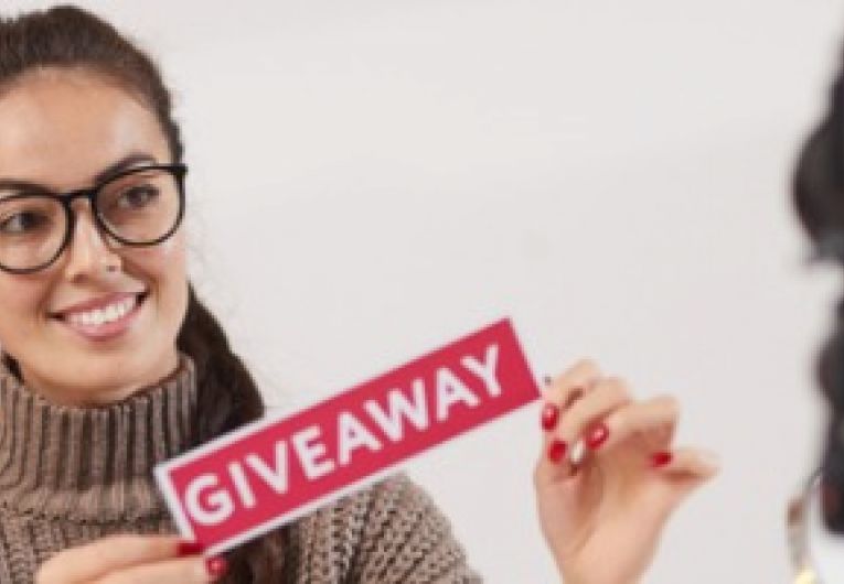 Entrepreneur holding up a giveaway sign while facing a video camera.