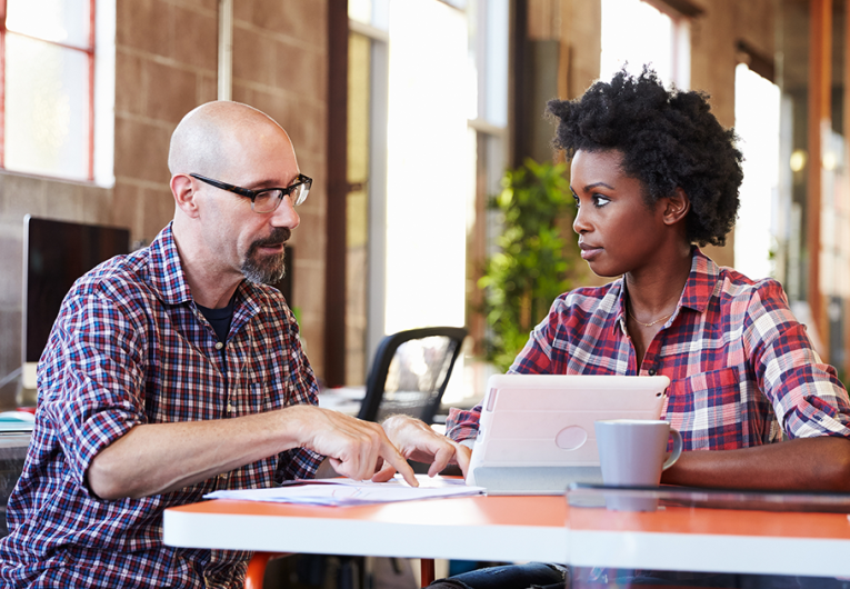 Two professionals sit at meeting table working on digital tablet