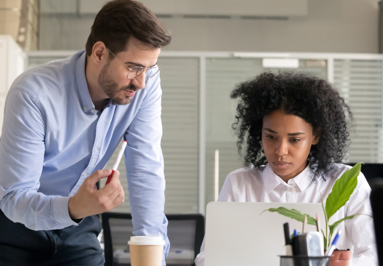 Business owner mentoring employee while they work on computer laptop