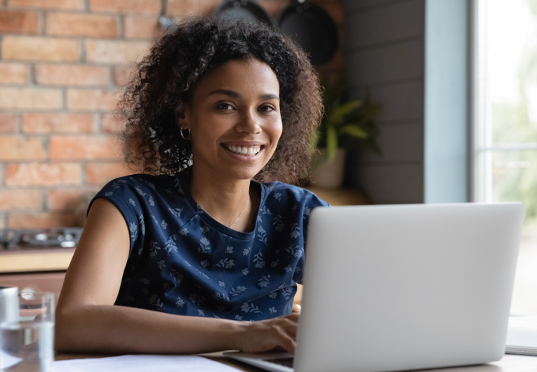 Positive motivated young female working on laptop smiling and looking at camera