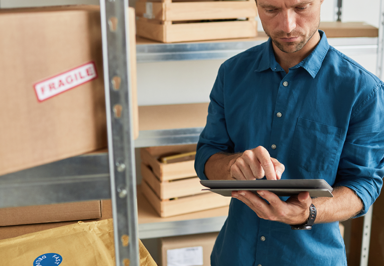 Waist up portrait of young man using digital tablet in warehouse while doing inventory and managing small business