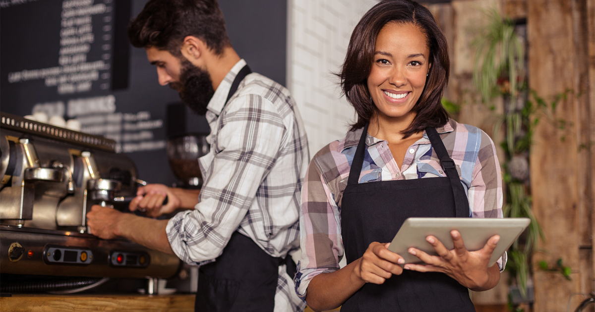 Waitress using a tablet computer and waiter with coffee machine in the bar