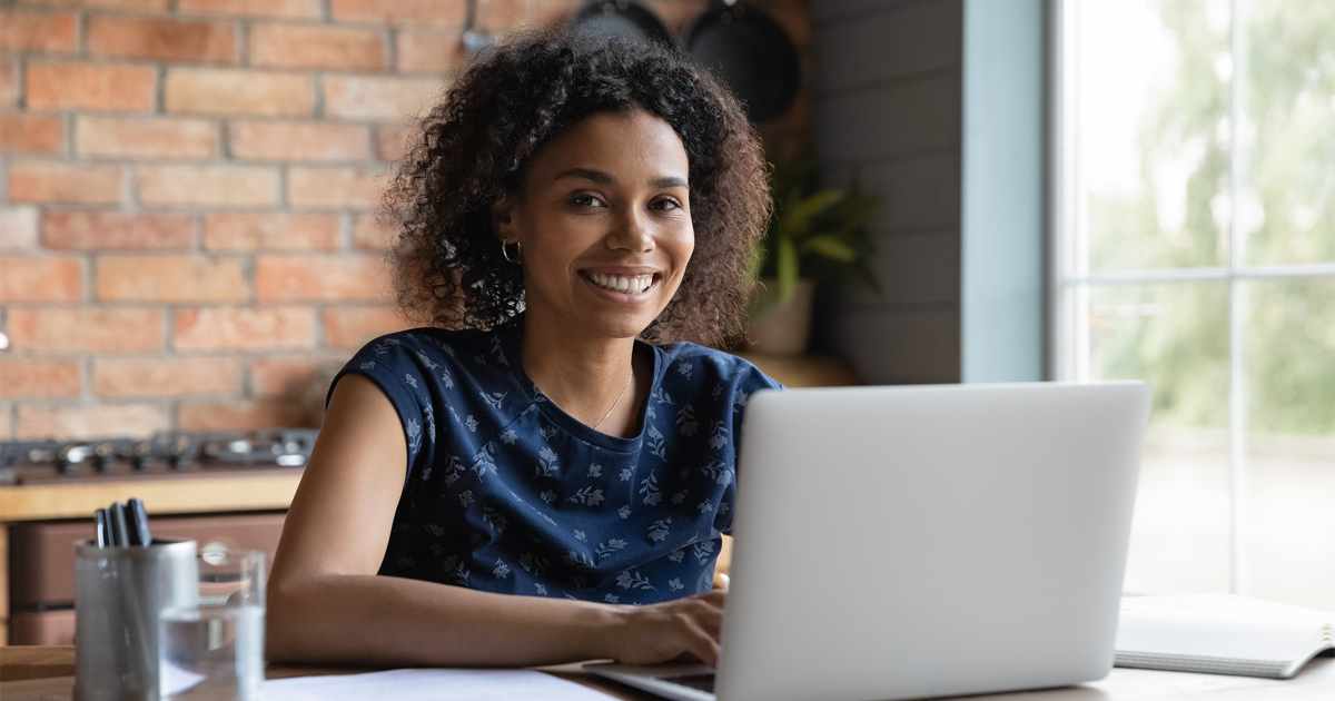 Positive motivated young female working on laptop smiling and looking at camera